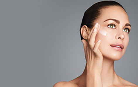 Model against a gray background swiping a serum onto her cheek. 