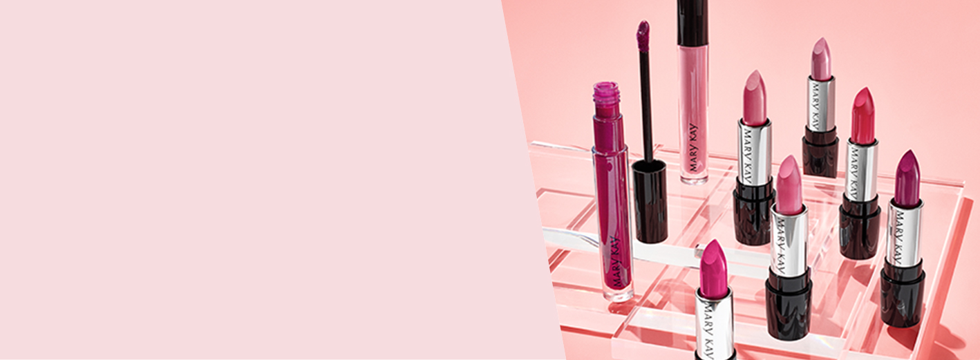 A group of red and pink Mary Kay lipsticks are photographed atop clear plexiglass squares in front of a pink background.