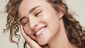 A picture of a smiling white woman in her twenties with curly hair and closed eyes