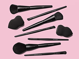 An assortment of Mary Kay brushes styled with Mary Kay Blending Sponges against a pink background.