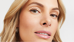 White blonde model with 60s styled hair and cut crease eyeshadow look, looking directly at the camera with a focus on her eye lid to show how to find crease line of eye lid with white line illustration to show eye lid crease line.