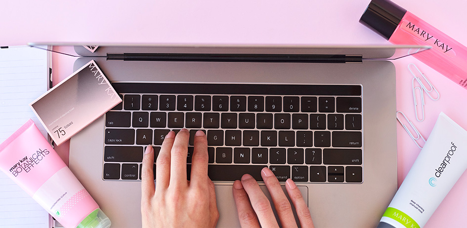 Женские руки печатают на ноутбуке в окружении продукции "Мэри Кэй"