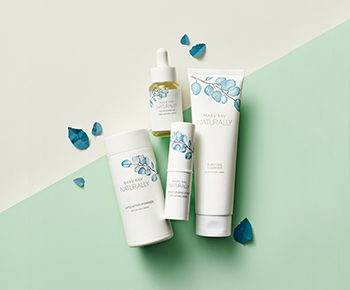The Mary Kay Naturally products in white packaging with teal leaf illustrations on a green background